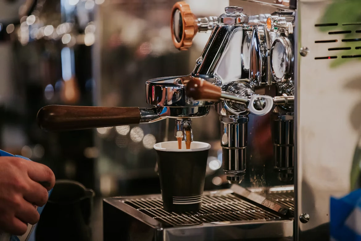 Warm light on a polished espresso machine pouring a shot into a black cup